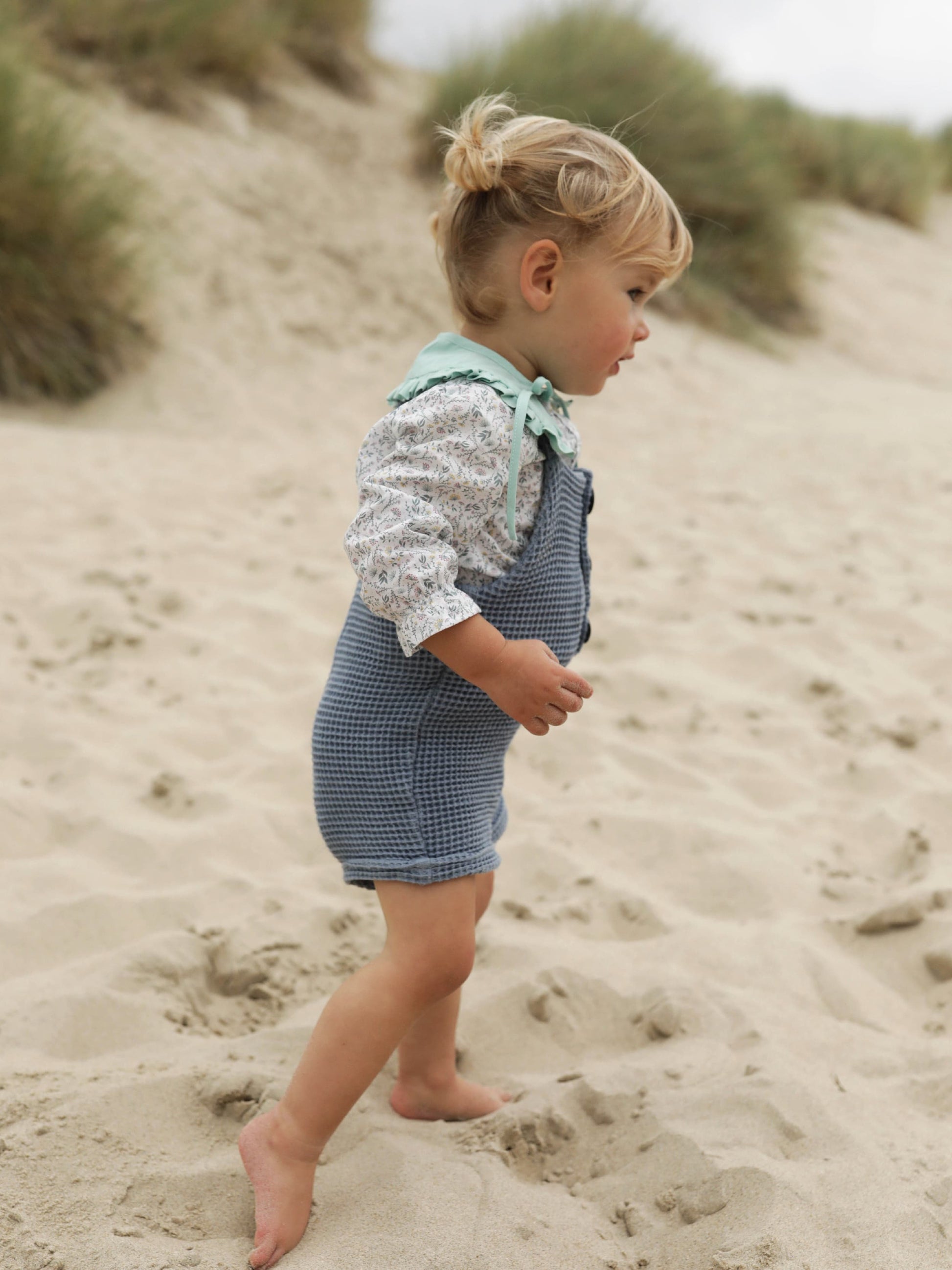 Petite fille en salopette dans le sable