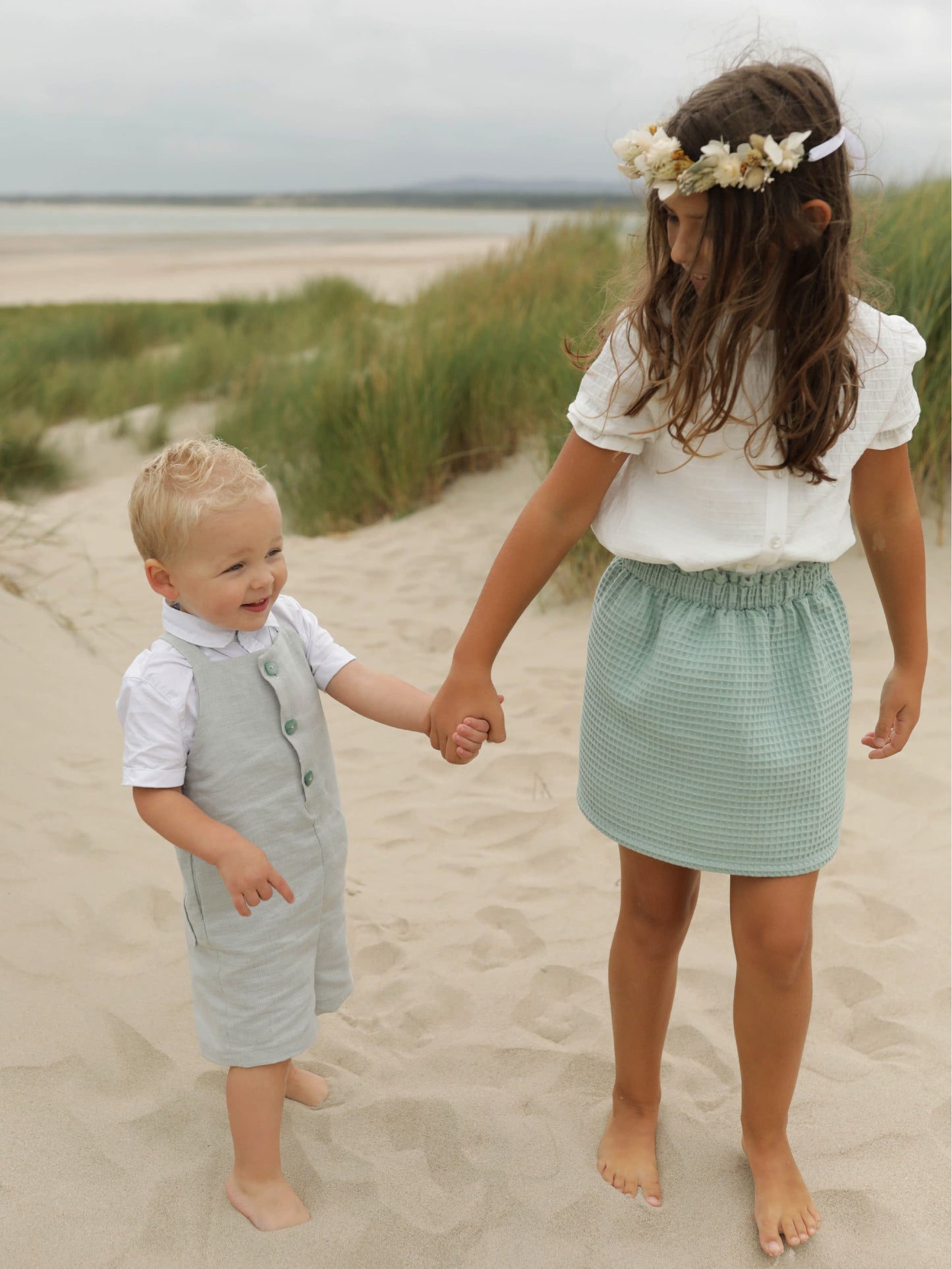 Petite fille en jupe qui tient la main à un petit garçon en salopette