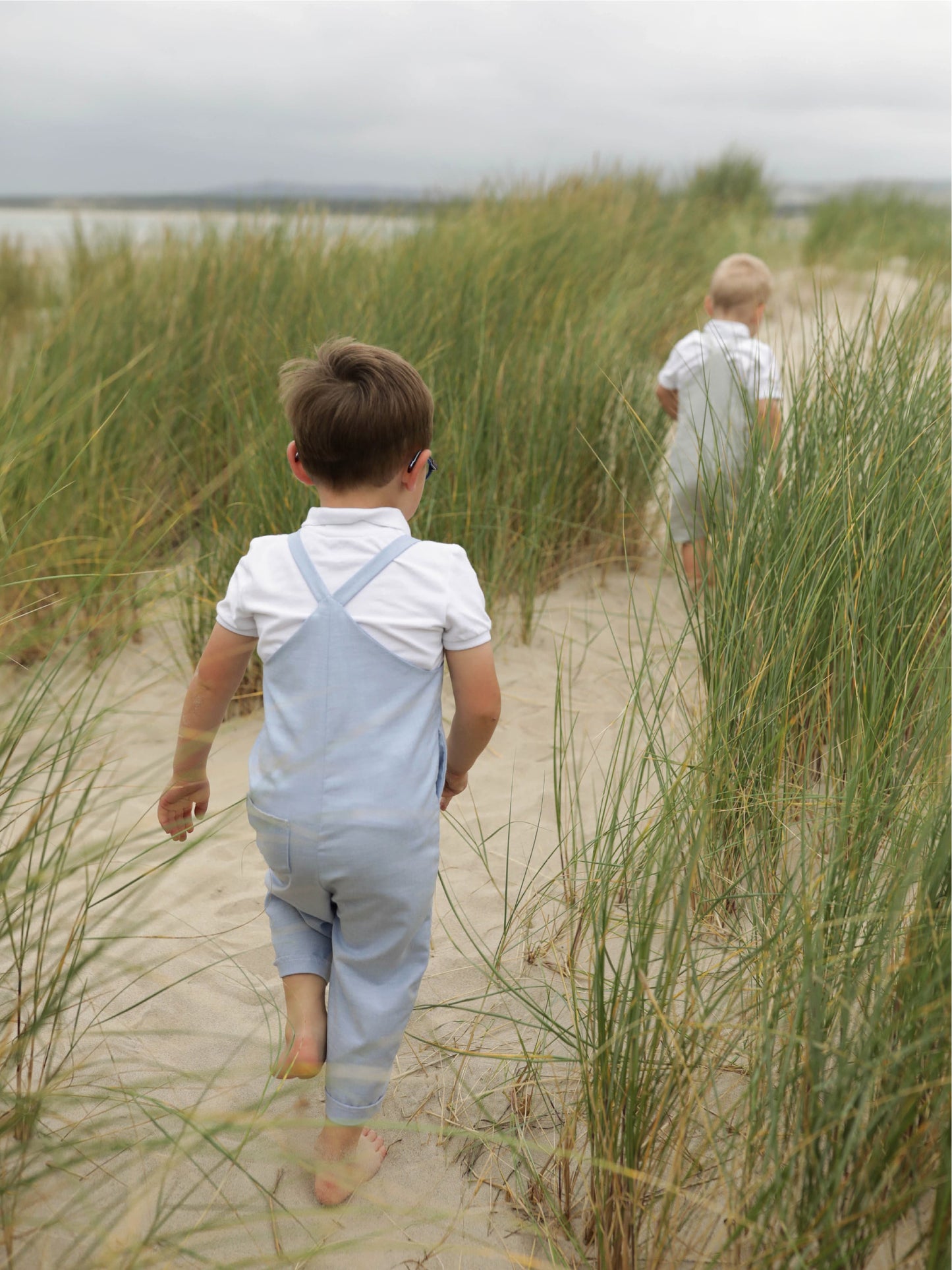 Petit garçon de dos en salopette marchant dans les dunes